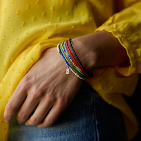 Close up of a woman wearing six different colored beaded bracelets on her wrist.