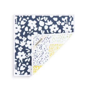 A double sided square dish cloth that is dark blue on one side with white floral illustrations, displayed with a corner turned back.