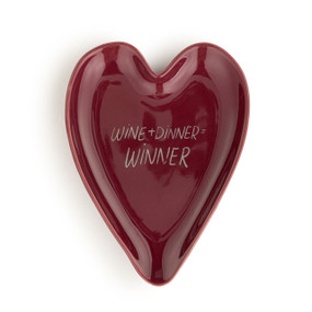 A dark red heart shaped ceramic spoon rest with the saying "Wine + Dinner = Winner" on it.