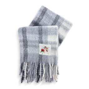A gray and white fringed blanket with a fabric patch that has a watercolor image of a hummingbird.