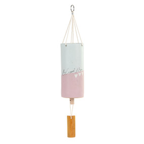 A pink and white tubular ceramic wind chime with a wood chime and three white hearts. The chime says "Blessed Mom".