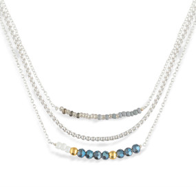 A layered silver necklace made of three different chains with gray and blue beads on them.