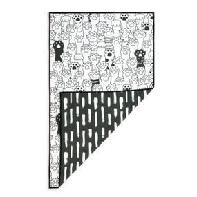 A rectangular double sided towel. One side is white with paw print illustrations and the other is black with short white lines, displayed with the black corner turned back.