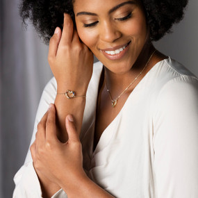 A smiling woman wearing a bracelet and necklace both with heart shaped charms containing small colored stones.