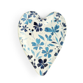 A white heart shaped ceramic spoon rest with a blue floral illustrations on it.