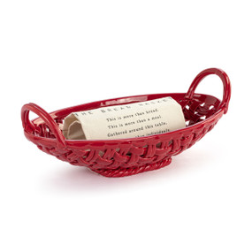 A red ceramic woven basket with handles on the ends and a cream towel inside with a saying about The Bread Basket.