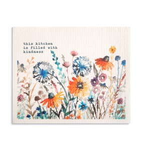 An oversized white biodegradable dish cloth with illustrated wildflowers and the saying "this kitchen is filled with kindness".