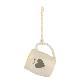 A cream ceramic mini mug that says "kind" with the image of a heart on the front, shown hanging with a coffee pod inside.