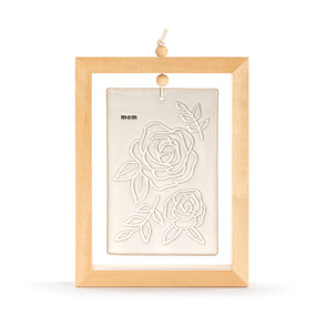 A cream ceramic plaque with roses and the word "mom" suspended inside a light wood open frame.