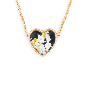 Detail view of the charm on an adjustable gold chain necklace with a heart shaped charm of white flowers on a dark background.
