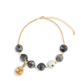 An adjustable gold chain bracelet with 7 black and white beads. There is a round gold charm that says "Believe Achieve" that can move between the seven beads.