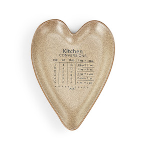 A dull gold heart shaped ceramic spoon rest with kitchen conversions on it.