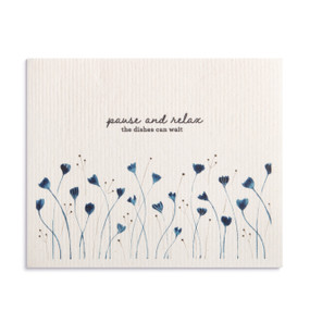An oversized white biodegradable dish cloth with blue flowers that says "pause and relax the dishes can wait".