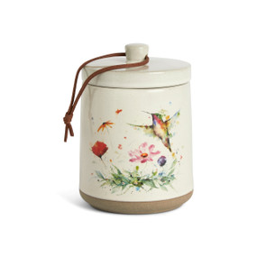 A cream ceramic candle with a tan textured base and a watercolor hummingbird and wildflowers on the outside with a removable lid.