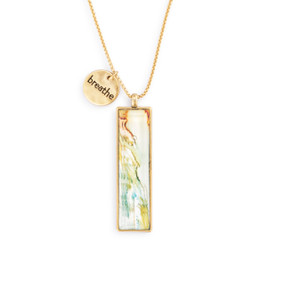 An adjustable gold chain necklace with a vertical gold charm with pastel abstract pattern artwork inspired by ArtLifting artist Alene Sirott-Cope. The necklace also has a small round gold token that says "breathe".
