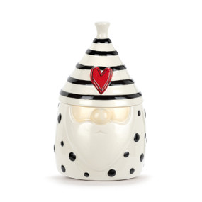 A white ceramic planter in the shape of a gnome. The main planter is white with black dots with the nose and beard of the gnome. The hat is a lid with black stripes and a raised red heart.