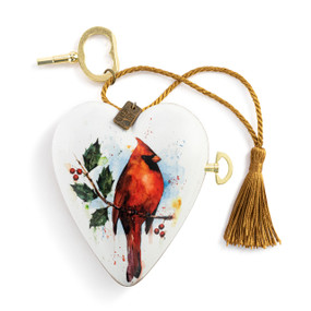 A white heart shaped musical sculpture with a watercolor image of a red cardinal. The heart has a gold tassel and gold key attached.