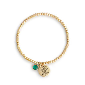 A gold beaded bracelet with a lily of the valley flower round charm and emerald colored stone.
