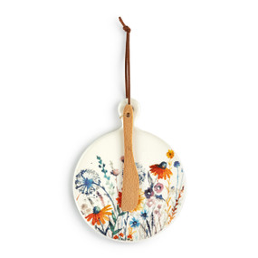 A round ceramic mini serving board with colorful meadow flowers. The board has a small wood knife attached.
