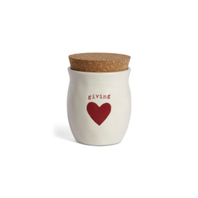 A cream ceramic container that says "giving" with a red heart and a cork lid. There is a poured candle inside.