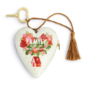 A heart shaped musical sculpture in a red and green home and floral pattern that reads "Family Makes the World Brighter". The heart has a bronze tassel and gold key attached.