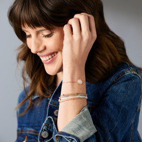 A woman wearing a multistrand bracelet with gold chains and beads in white and pink.