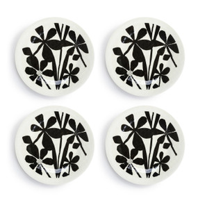A set of four white melamine appetizer plates with a black floral pattern in the middle, displayed set out next to each other.