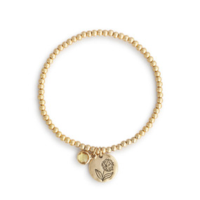 A gold beaded bracelet with a chrysanthemum round charm and topaz colored stone.