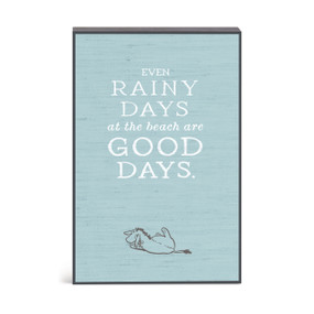 A blue wall art with an illustration of Eyeore and the saying "Even rainy days at the beach are good days".