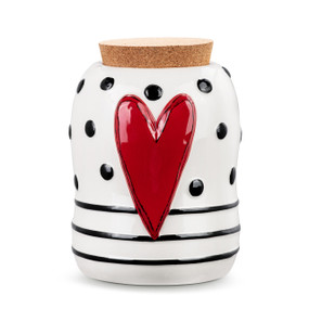 A white ceramic canister with black dots and stripes and a raised red heart on the front. The canister has a cork lid.