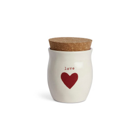 A cream ceramic container that says "love" with a red heart and a cork lid. There is a poured candle inside.