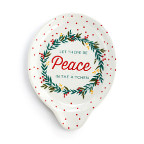 Top down view of a white ceramic spoon rest with a green wreath, red dots and the saying "Let There Be Peace In The Kitchen".