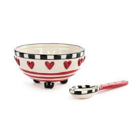 A white, black and red ceramic candy dish with matching spoon. There are raised red hearts around the bowl and black feet.