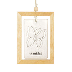 A hanging cream ceramic plaque with a butterfly and the word "thankful" suspended inside a light wood open frame.