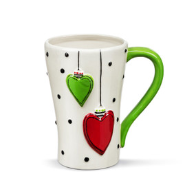 A white ceramic mug with a green handle and two raised heart ornaments in red and green on the front.