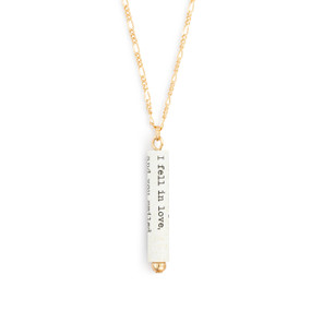 A gold chain necklace with a white scroll charm. The scroll has a saying from William Shakespeare.