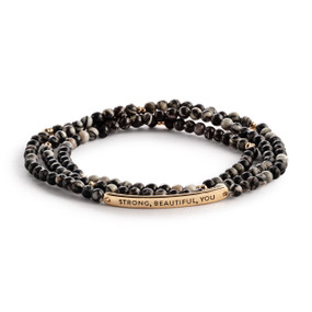 A multi-strand beaded bracelet in black with a gold metal bar that says "Strong, Beautiful, You".