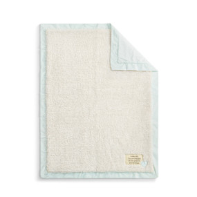 A plush cream blanket with a light blue edge and back. There is a fabric patch in the bottom right corner.