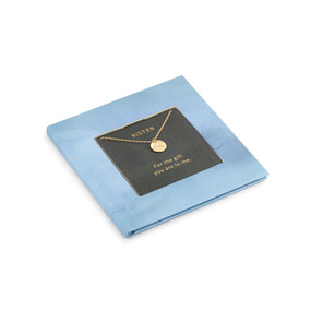 A small square blue book with inspirational content about sisters. There is a gold chain necklace inside with a round charm.