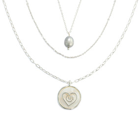 Detail view of the charms on a three strand silver necklace with a round heart charm on the longest strand.