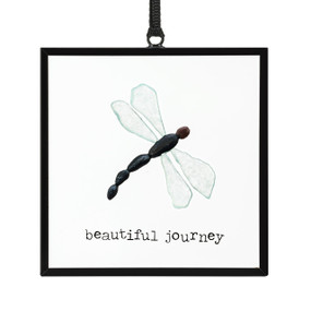 A small square suncatcher with a dragonfly made out of small colored stones and the saying "beautiful journey".