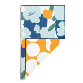 A rectangular double sided towel. One side is white with large blue flower illustrations and the other is orange with large white circles, displayed with the orange corner turned back.