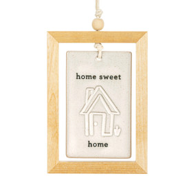 A hanging cream ceramic plaque with a home and the saying "home sweet home" suspended inside a light wood open frame.