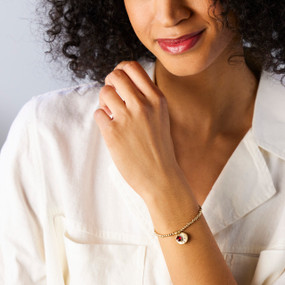 A woman wearing a gold chain bracelet with a birthstone charm and stone for the month of July.