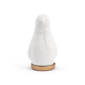 A white ceramic diffuser shaped like a penguin wearing a scarf resting in a round gold shallow dish.