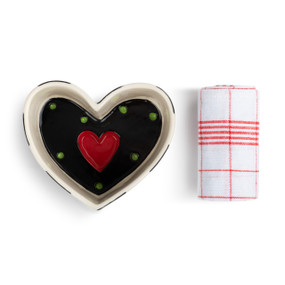 A small heart shaped ceramic pan with a black interior with a red heart and green dots. The pan comes with a white towel with red stripes.