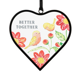 A small heart shaped sun catcher with an illustration of two birds perched on red and yellow flowers and the saying "Better Together".