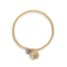 A gold beaded bracelet with a holly leaf round charm and blue colored stone.