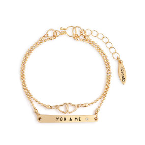 An adjustable gold layered bracelet with intertwined hearts on one layer and a band that says "You & Me" on the other.