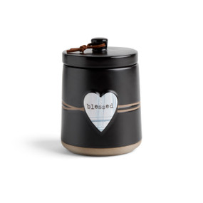 A round black ceramic poured candle with a tan textured base, a lid and a white raised heart on the front with thin blue lines and the words "blessed".